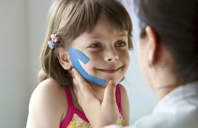 Woman applies kinesiology tape to girl's cheek